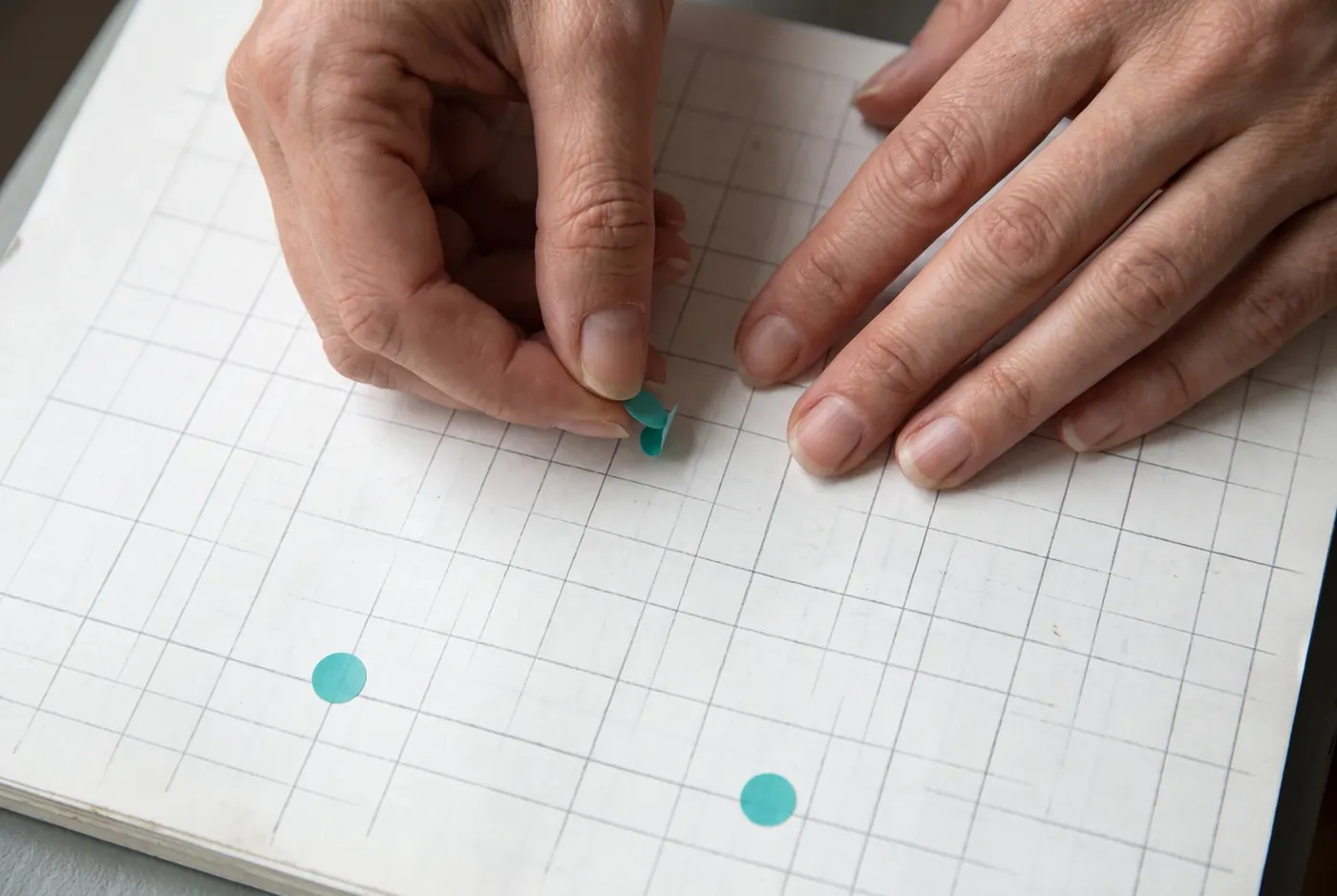 Hands moving a dot sticker on a blank paper grid