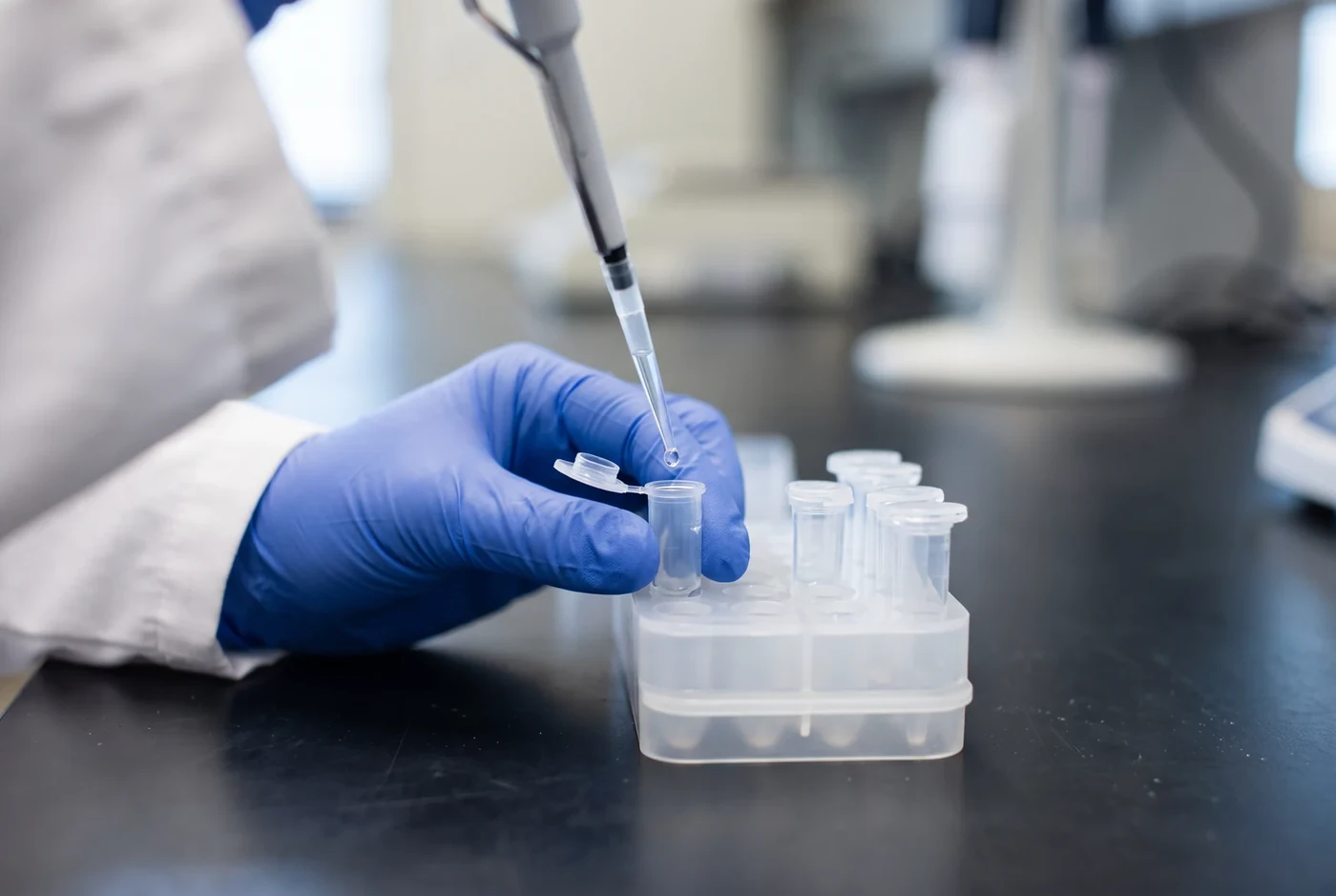 Gloved hand pipetting a clear sample into a tube